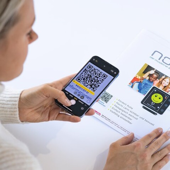 Eine Person scannt mit ihrem Smartphone einen QR-Code auf einem Informationsblatt, das ein Etikett mit QR-Code trägt und Details zu einem Produkt enthält.