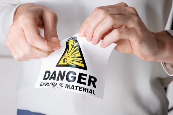 Eine Person entfernt einen Aufkleber mit dem Warnhinweis „Achtung: Explosives Material“ und dem dazugehörigen Symbol.