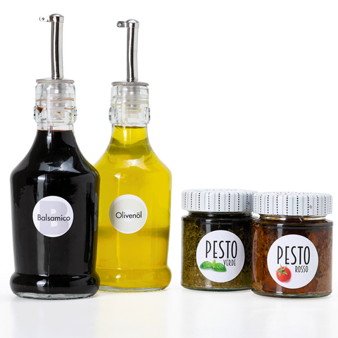 Zwei Flaschen Balsamico und Olivenöl sowie zwei Gläser Pesto in verschiedenen Sorten vor einem weißen Hintergrund.
