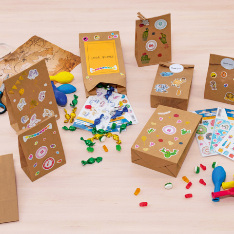 Bunte Geschenktüten und Bastelmaterialien auf einem Tisch, darunter Aufkleber, Luftballons, Scheren und Süßigkeiten."
(Note: The text is already in German and does not require translation. It is clear and fluent as it is.)