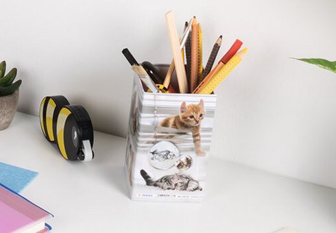 Ein Stiftehalter mit Katzenmotiven, gefüllt mit verschiedenen Schreibutensilien, steht auf einem Schreibtisch.