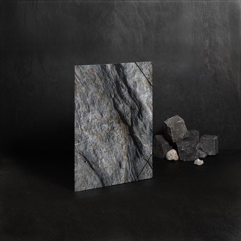 Eine graue Steinplatte steht aufrecht, daneben liegen mehrere kleinere Steine. Der Hintergrund ist dunkel und einheitlich.