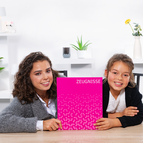 Zwei Mädchen sitzen an einem Tisch und halten ein pinkes Heft mit der Aufschrift 'ZEUGNISSE'. Sie lächeln in die Kamera."
(Note: The original text is already in German and does not require translation. It is clear and fluent as it stands.)