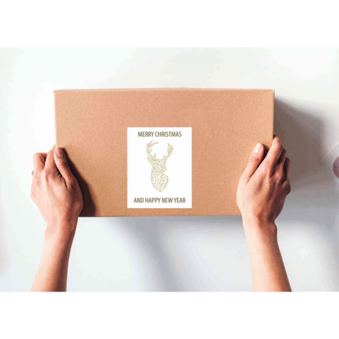 Eine Person hält ein braunes Paket mit einem Aufkleber, der "Frohe Weihnachten und ein glückliches neues Jahr" zeigt, dekoriert mit einem Geweih.