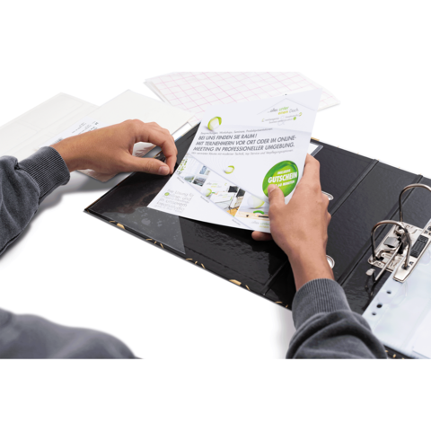 Eine Person hält ein Dokument mit dem Wort "Gutschein" und arbeitet an einem Tisch mit einem Ordner und weiteren Unterlagen.