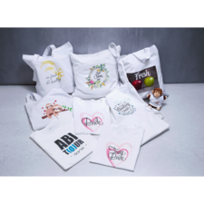 Verschiedene weiße Taschen und Kissen mit bunten Aufdrucken, darunter "Bride" und "Fresh", sowie ein kleiner Stoffaffe.