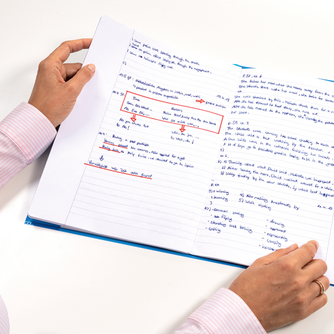Eine Person hält ein aufgeschlagenes Notizbuch mit handschriftlichen Notizen und Markierungen in blauer und roter Tinte."
(Note: The text is already in German and does not require translation. It is clear and fluent as it is.)