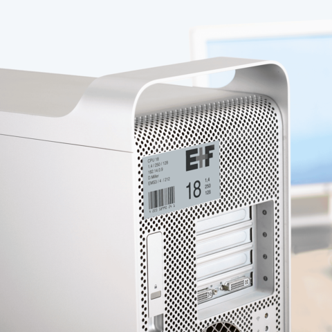 Silberner Computer mit perforierter Rückseite, ausgestattet mit mehreren Anschlüssen und einem Aufkleber mit technischen Spezifikationen.