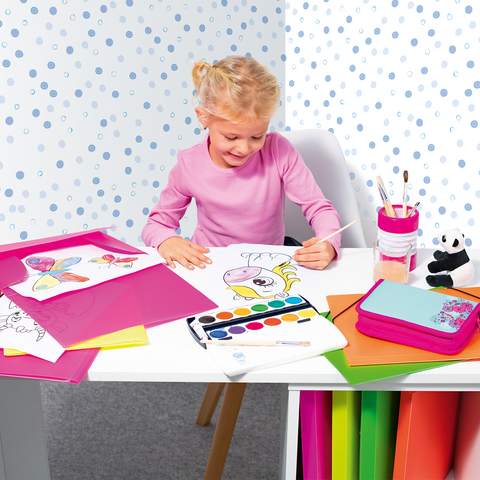 Ein kleines Mädchen sitzt an einem Tisch, malt mit Wasserfarben und ist umgeben von buntem Papier und ihren Zeichnungen.