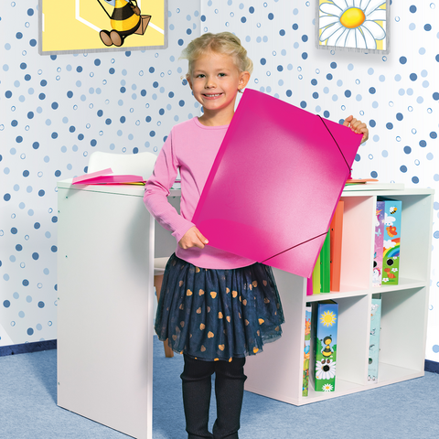 Ein kleines Mädchen sitzt an einem Tisch, malt mit Wasserfarben und ist umgeben von buntem Papier und ihren Zeichnungen.