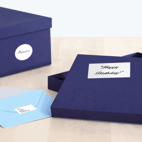 Eine geöffnete, dunkelblaue Geschenkbox mit der Aufschrift "Happy Birthday!" und zwei Umschlägen in verschiedenen Farben daneben.