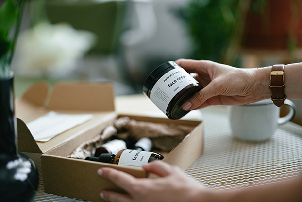 Ein beschlagenes Fenster mit einem Warnschild, eine Person öffnet eine Box mit Behältern, während eine andere Person ein Gefahrenetikett abnimmt.