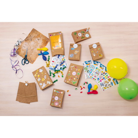 Bastelmaterialien auf einem Tisch, darunter braune Umschläge mit Aufklebern, Scheren, Bänder, Luftballons und Bastelblätter.