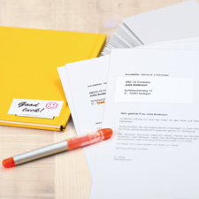 Ein gelbes Ordnerset mit einem Aufkleber "Viel Glück!" und Dokumenten, die an die ABCD-15 Company adressiert sind, liegen auf einem Tisch.
