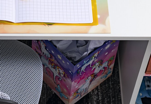 Bunter Papierkorb mit Einhorn-Motiv unter einem Schreibtisch.