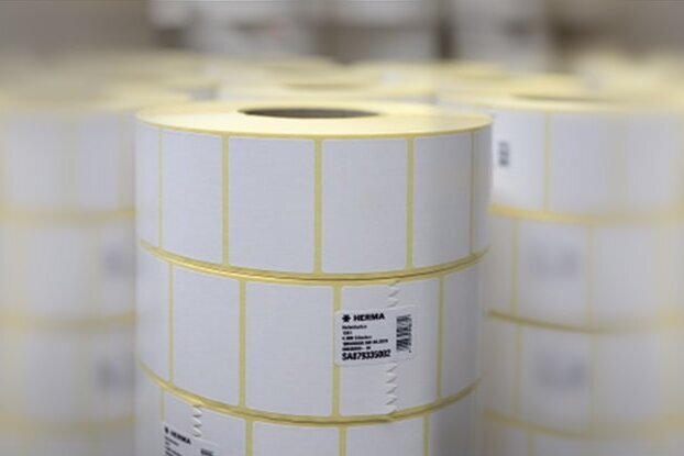 Rollen mit weißen Etiketten, übereinander gestapelt in einem Lager. Die Etiketten sind mit gelben Linien gekennzeichnet.