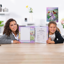 Zwei Mädchen sitzen an einem Tisch und halten ein offenes Heft mit einem Zertifikat sowie einem leeren Blatt. Im Hintergrund sind dekorative Elemente zu sehen.