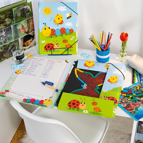 Ein Schreibtisch mit bunten Schulmaterialien, darunter Hefte, Stifte, eine Lampe und eine Vase mit einer Blume.