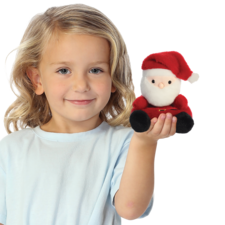 Ein Kind mit blonden Locken hält eine kleine, plüschige Weihnachtsmannfigur in der Hand und lächelt freundlich.