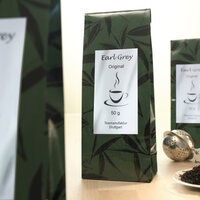 Earl Grey Tee in einer grünen Verpackung mit einem Etikett, das den Inhalt und das Gewicht von 50 g angibt." 

(Note: The text is already in German and does not require translation. It is clear and fluent as is.)