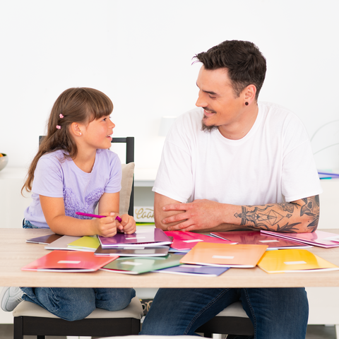 Ein Mann und ein Mädchen sitzen an einem Tisch, umgeben von bunten Farbmusterkarten, und scheinen ein Gespräch zu führen.