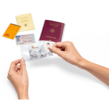 Eine Hand hält eine transparente Hülle mit einer ID-Karte, während im Hintergrund ein Reisepass und mehrere Ausweisdokumente liegen.