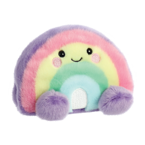 Buntes, kuscheliges Regenbogen-Kissen mit lächelndem Gesicht und runden, lila Pompons an den Enden.