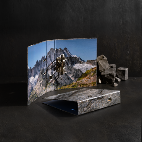 Ein Ordner mit einem Berglandschaftsdesign, geöffnet und auf einem dunklen Untergrund platziert, neben einigen Steinen.