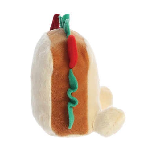Plüsch-Hotdog mit bunten Zutaten, seitlich betrachtet. Der Hotdog hat eine helle Wurst und grüne sowie rote Akzente.