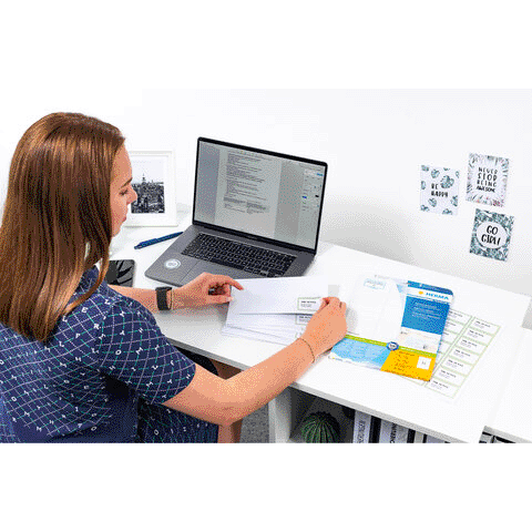 Eine Person sitzt an einem Schreibtisch und arbeitet am Laptop, umgeben von Dokumenten und Notizen.