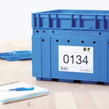 Blaue Kunststoffbox mit einer Etikette, die die Nummer 0134 zeigt. Daneben ein Notizblock und ein blauer Stift auf einem Tisch.