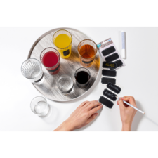 Ein Tablett mit verschiedenen Getränken in Gläsern und einer Hand, die mit einem weißen Stift auf schwarzen Etiketten schreibt.