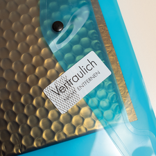 Transparente Hülle mit einem schwarzen, gewellten Innenmaterial und einem Aufkleber, der "Vertraulich" und "Entfernen" zeigt.