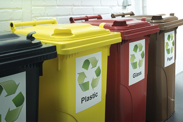 Fläschchen mit Flüssigkeiten, verschiedene Recyclingbehälter für Abfälle und eine Person, die ein Warnschild für gefährliche Stoffe anbringt.