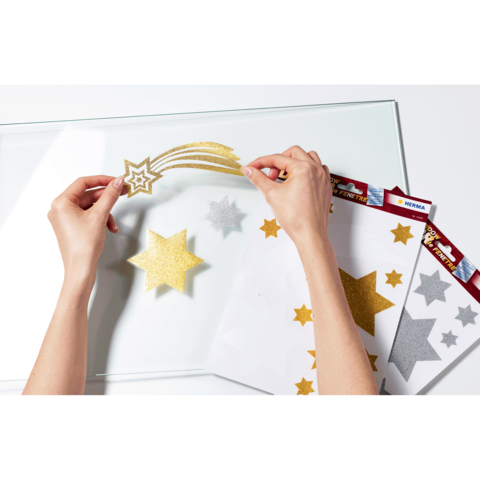 Hände platzieren goldene und silberne Glitzersterne auf einer transparenten Oberfläche, um eine Dekoration zu gestalten.
