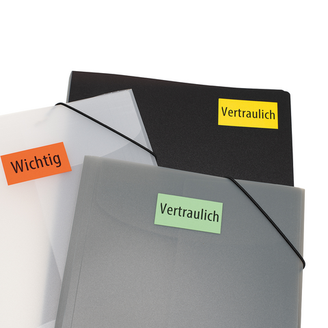 Kartonbox auf einem Tisch mit einem roten Heft und einem grünen "TOP"-Aufkleber. Im Hintergrund sind Bücherregale sichtbar.