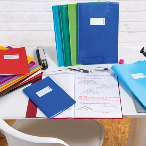 Eine Frau und ein kleines Mädchen sitzen an einem Tisch und blättern durch ein Heft, umgeben von Schreibmaterialien.