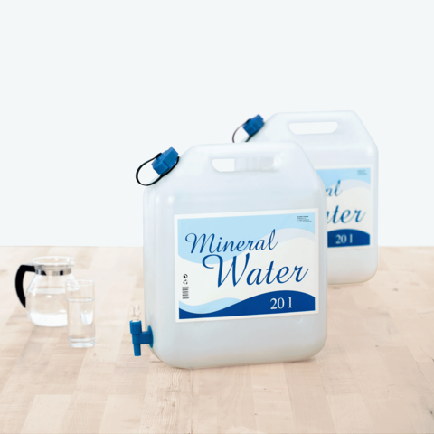 Zwei große Behälter mit Mineralwasser, jeweils 20 Liter, stehen auf einem Tisch neben einem Krug und einem Glas.
