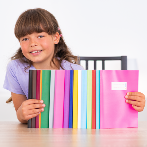 Ein Mädchen hält eine Reihe von bunten Heften in verschiedenen Farben, lächelnd und in einem hellen Raum sitzend.