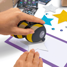 Eine Hand nutzt einen Stempel, um einen Stern auf ein Blatt Papier zu drucken, das von bunten Sternen und Dekorationen umgeben ist.