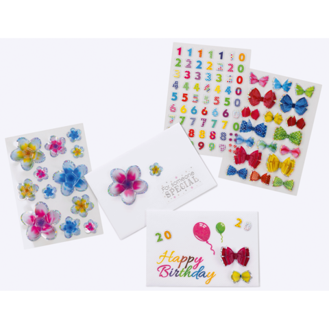 Bunte Aufkleber mit Blumen, Zahlen und Schleifen, sowie eine Geburtstagskarte mit der Aufschrift "Happy Birthday" und Luftballons.