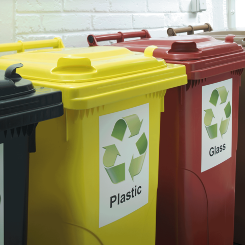 Drei Abfallbehälter in verschiedenen Farben für Recycling: Gelb für Plastik, Rot für Glas und Schwarz für Restmüll.