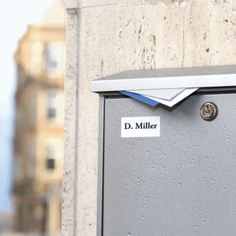 Graue Briefkasten mit dem Namen "D. Miller" auf einem urbanen Hintergrund.