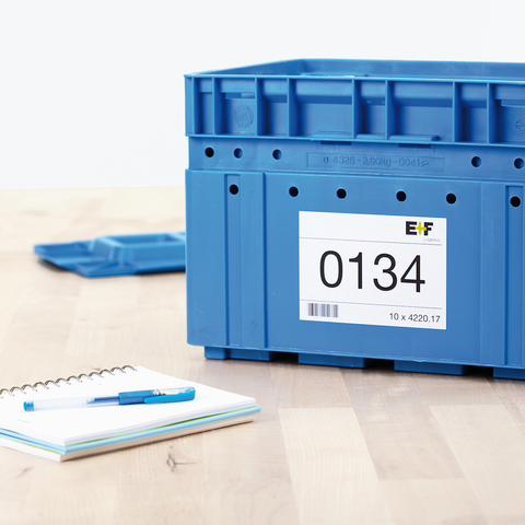 Blaue Kunststoffbox mit der Aufschrift "0134" und einem Etikett, daneben ein Notizblock und ein blauer Stift auf einem Tisch.